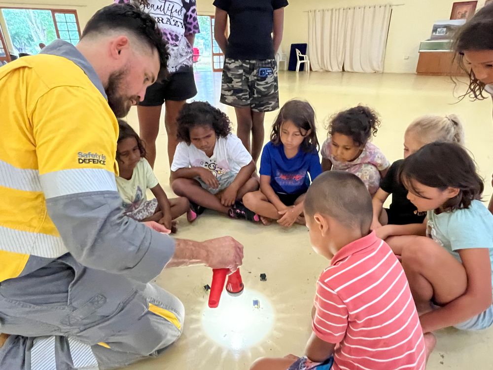 Ergon Energy Network worker on floor with children and a torch