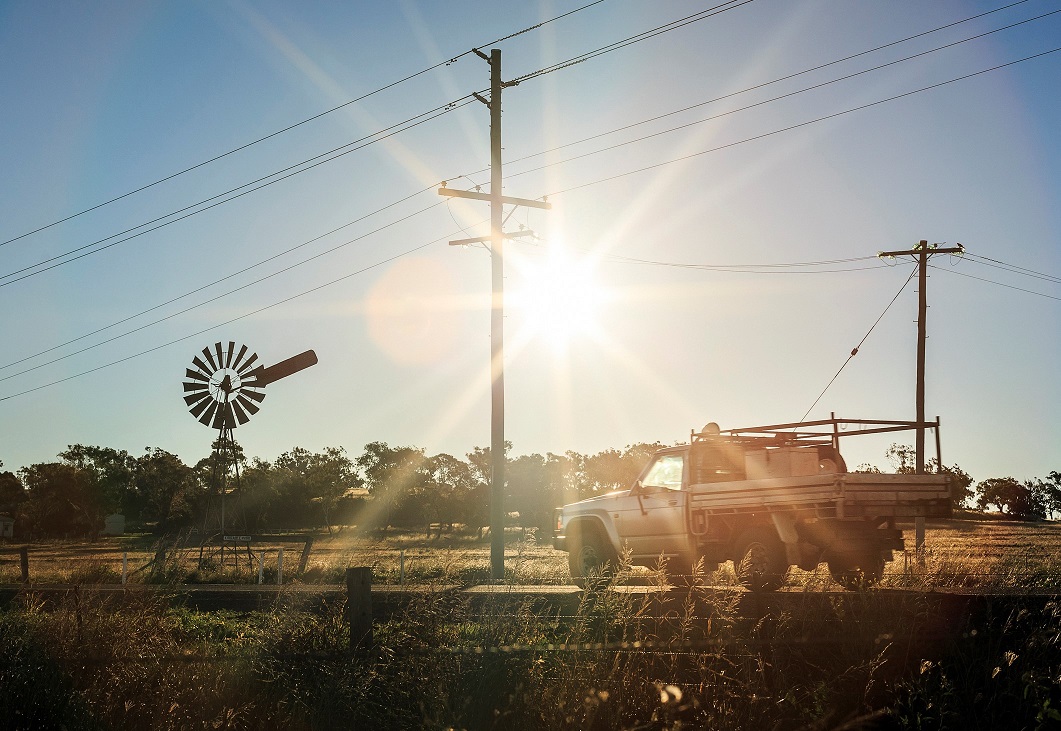 Ute on the road passing a windmill in a paddock