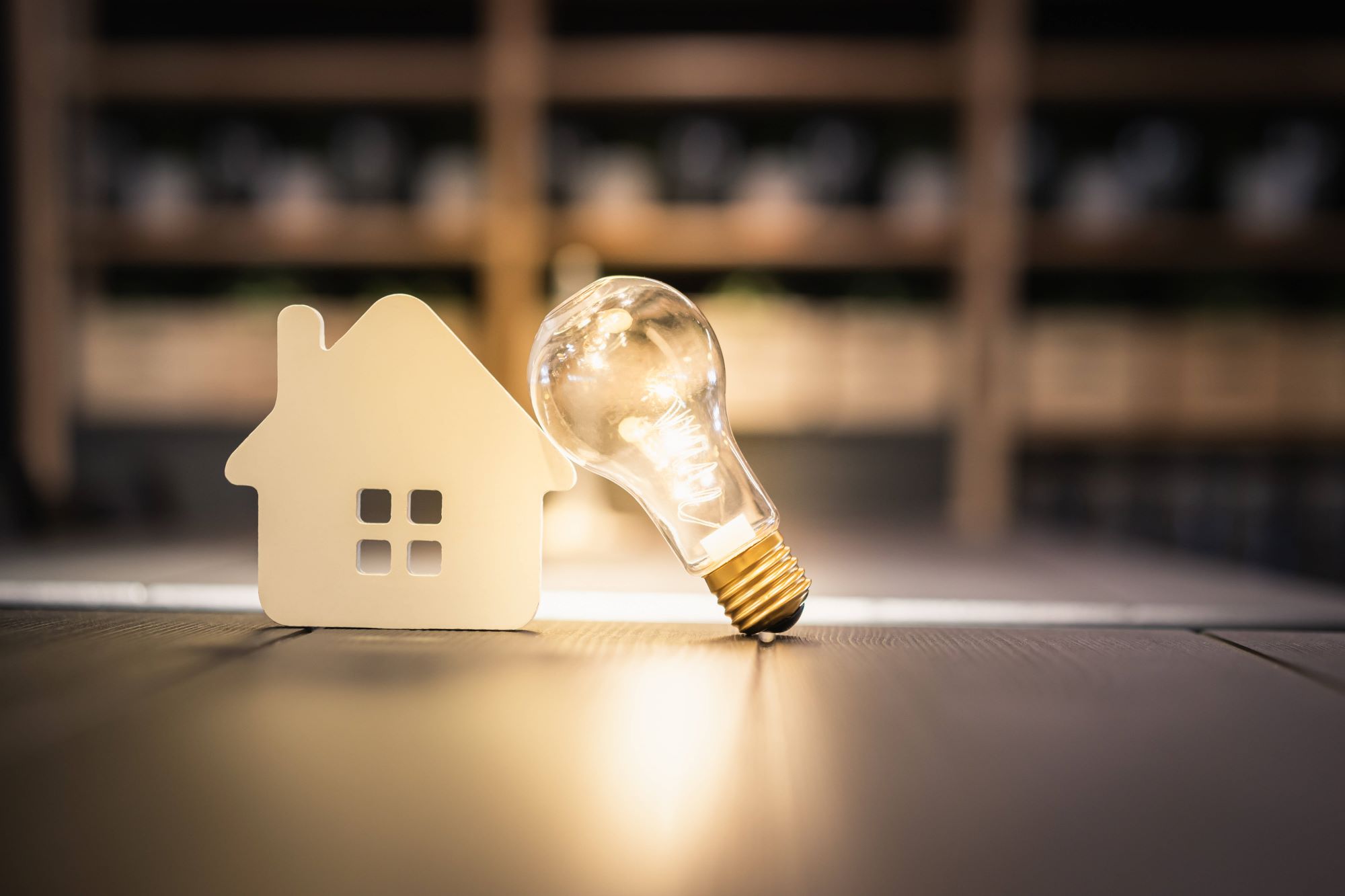 Mini house with light bulb leaning against roof on table