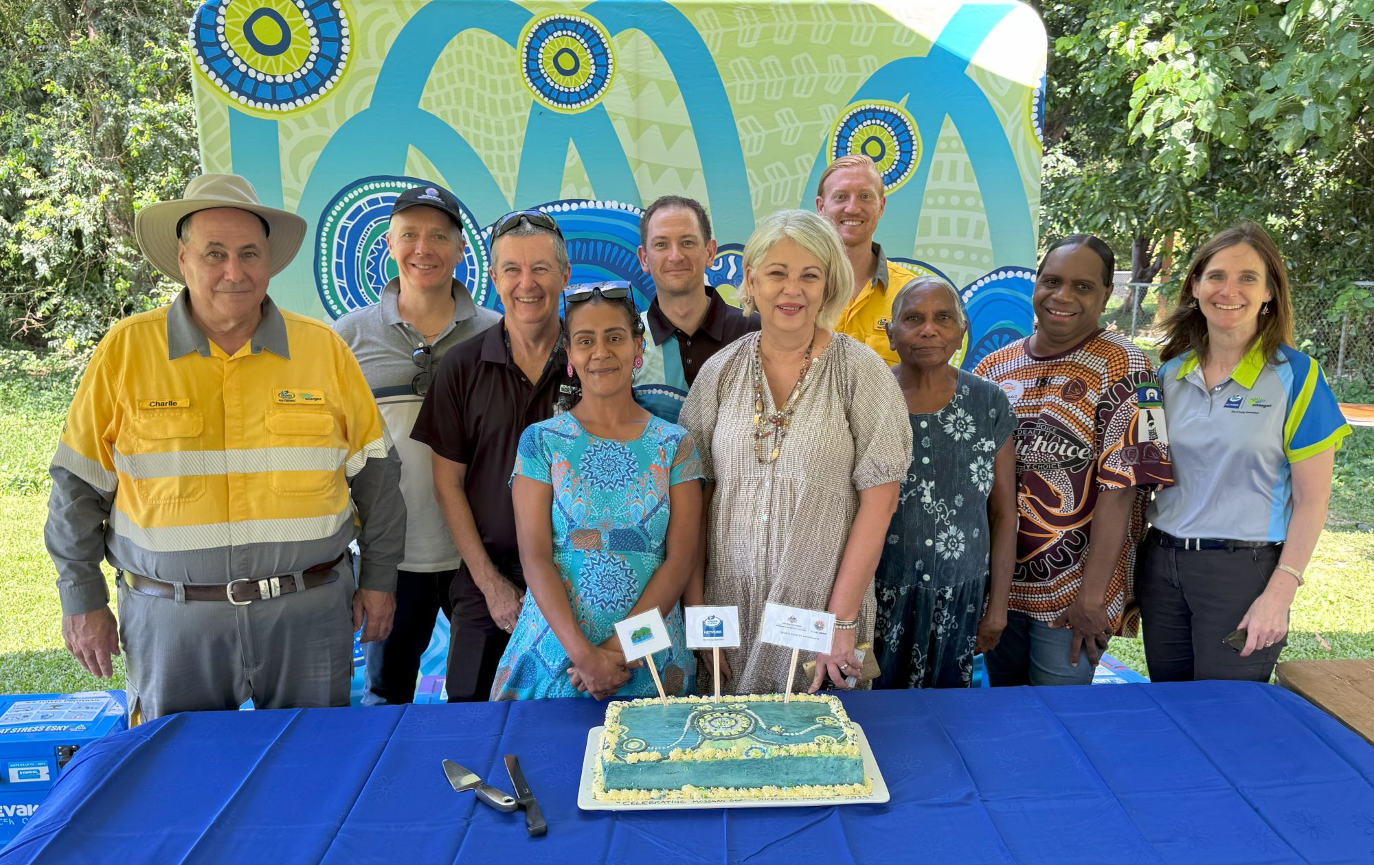 Group of people in front of cake on table celebrating the launch of the Mossman Gorge Microgrid Project