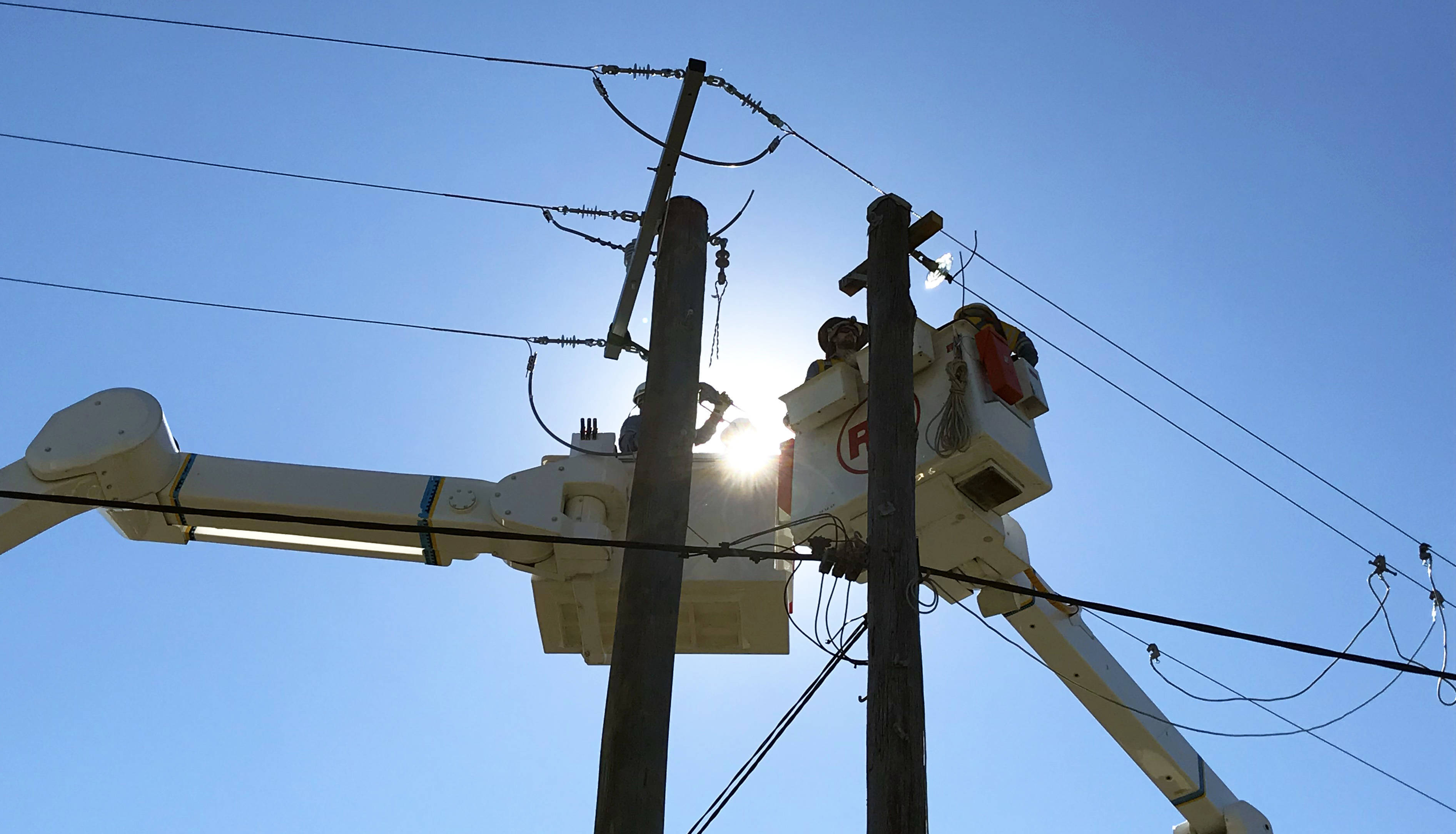 Crews working in a bucket truck at the top of a power pole