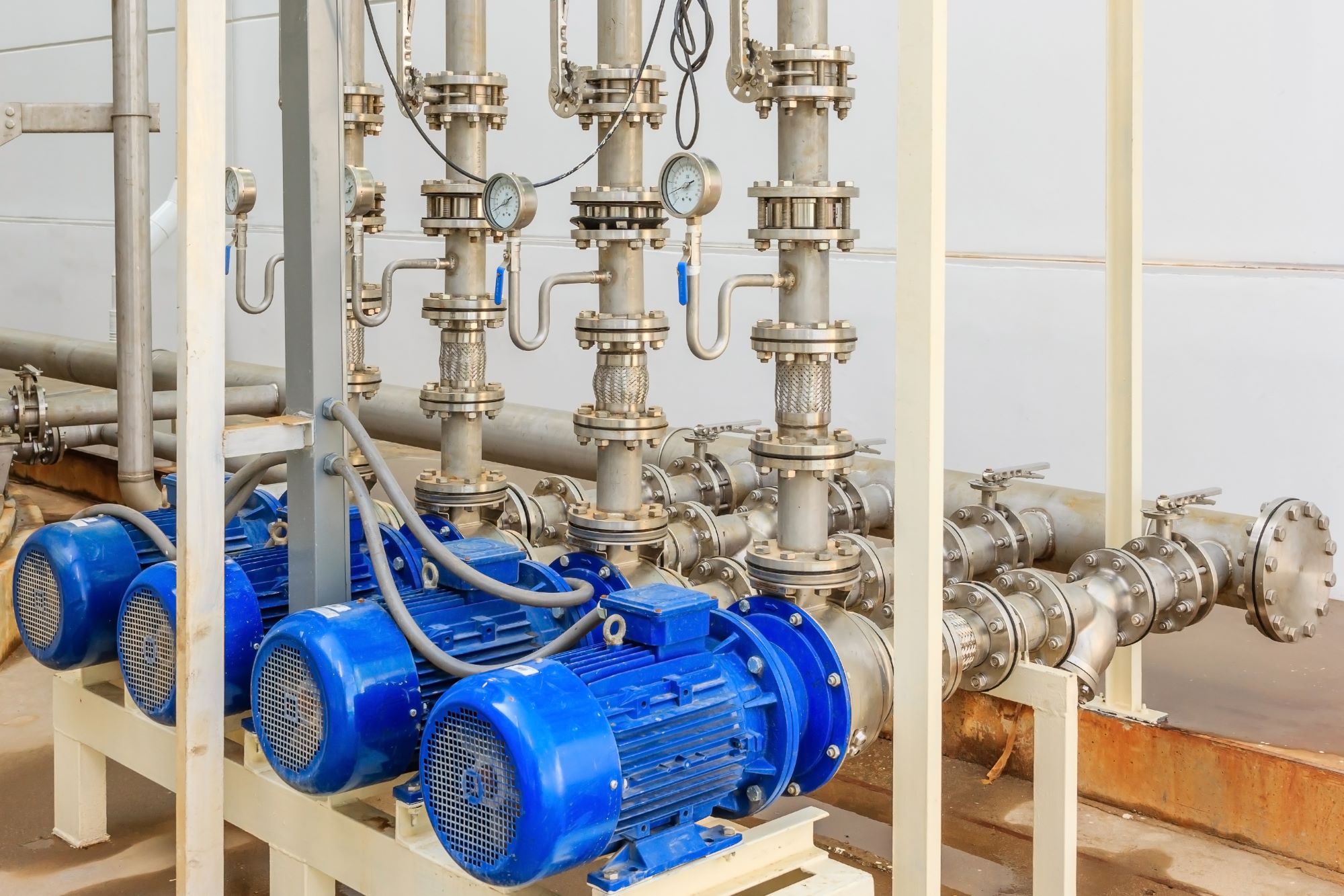 Large industrial water treatment and boiler room. Shiny steel metal pipes and blue pumps and valves.