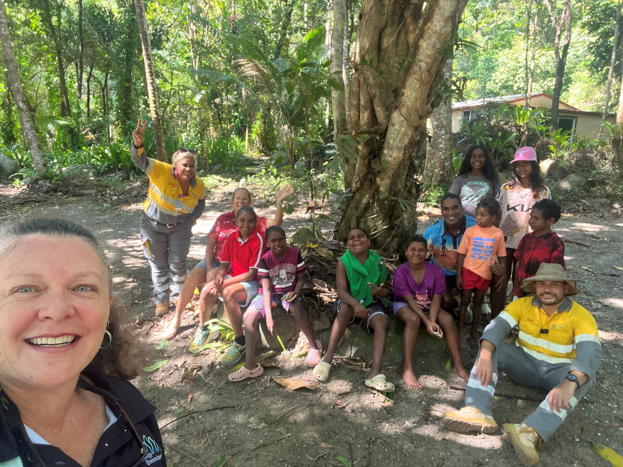 Group of children with Ergon Energy employees under a tree